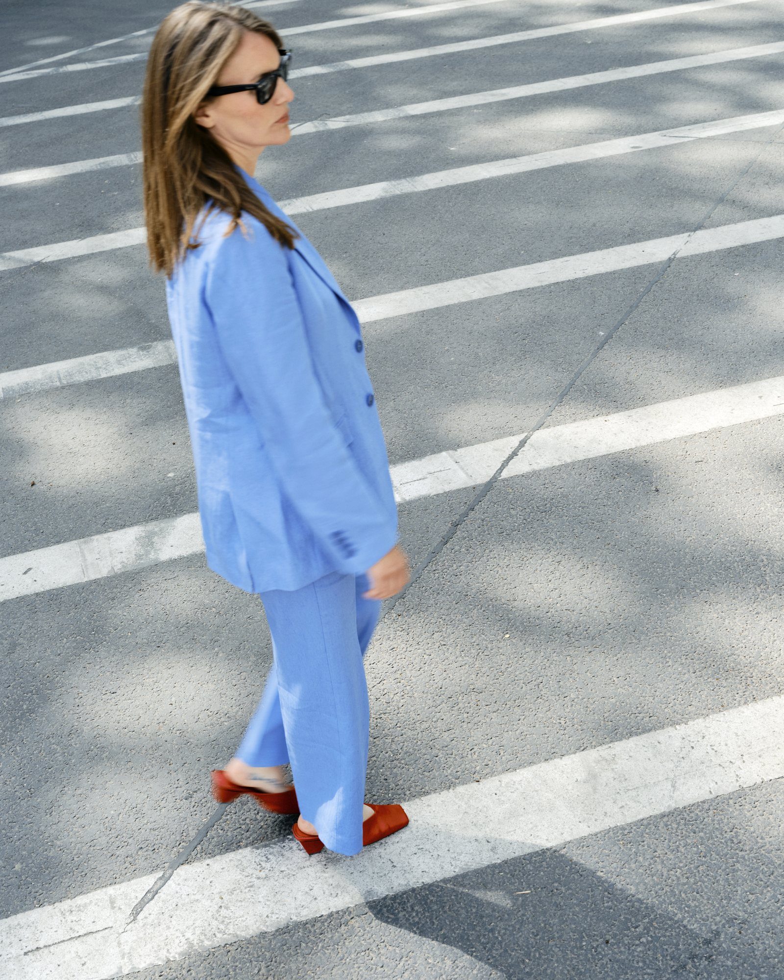 Julia Krummhauer mit Sonnenbrille im blauen Anzug auf einem Zebrastreifen